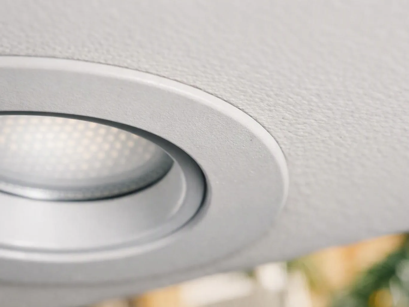 Close-up of a recessed ceiling light set into a textured white panel with soft blurred background colors