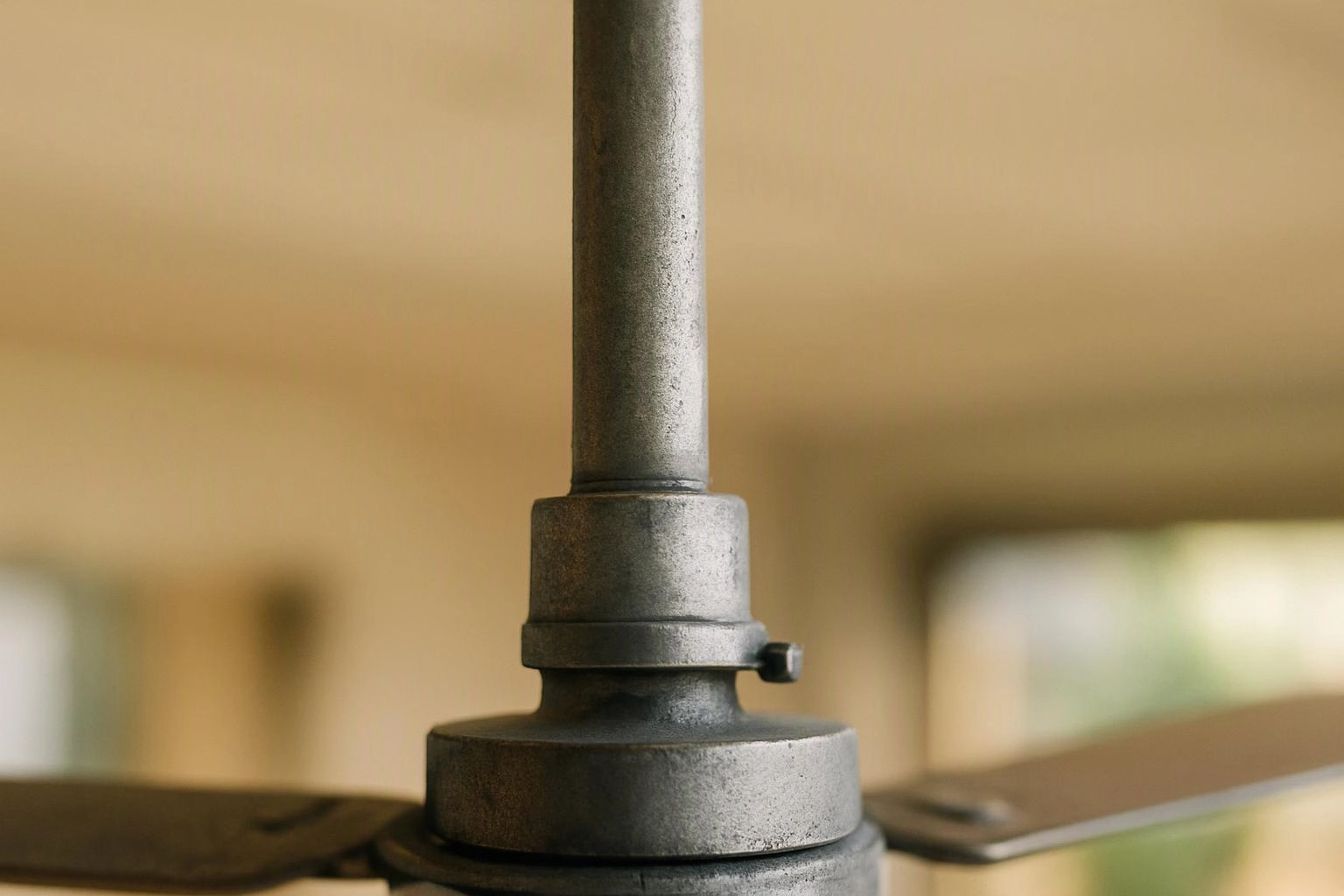 A close-up of a metal ceiling fan mount and rod against a blurred indoor background